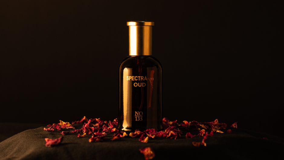 Elegant oud perfume bottle surrounded by rose petals on a dark backdrop, exuding luxury.