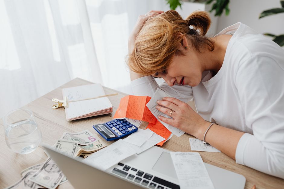 A woman overwhelmed with finances, surrounded by bills, calculator, and cash at home.