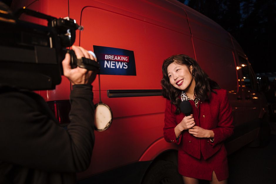Asian female reporter in a red blazer reporting live on the news outdoors in the evening.