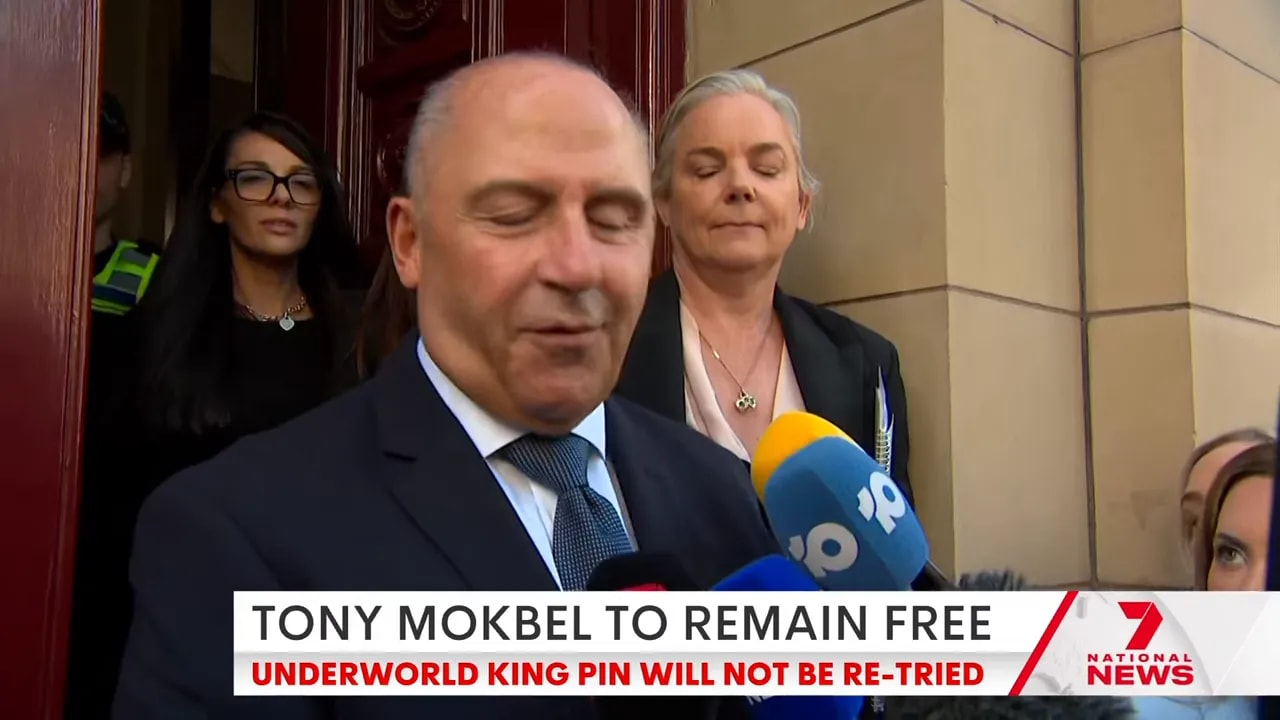 Man giving a statement to reporters at the courthouse steps with multiple microphones in view