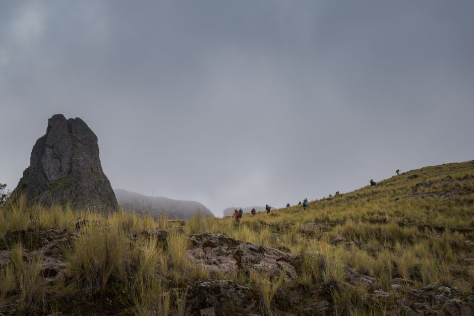 Group of hikers trekking on a mountain trail in the Andes, Cusco, Peru on a cloudy day.