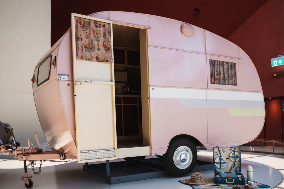 A retro pink caravan on display indoors with an open door, evoking nostalgia and travel.