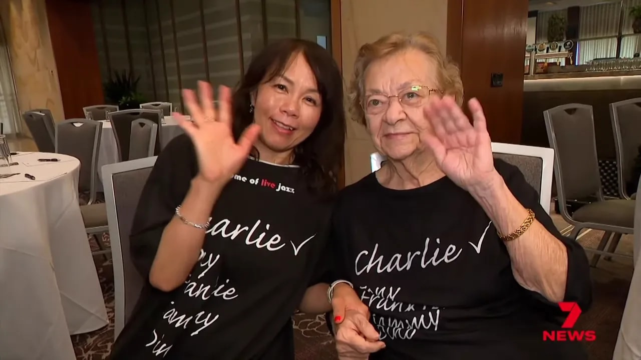 Two fans wearing matching 'Charlie' T-shirts waving at the camera inside a venue