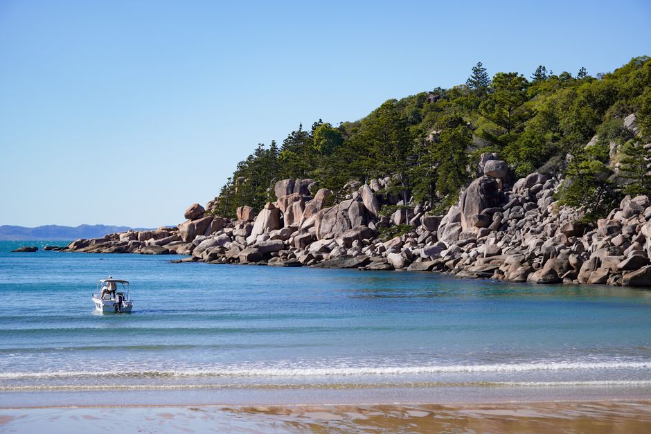 Tranquil beach scene with a small boat near rocky coastline and lush greenery.