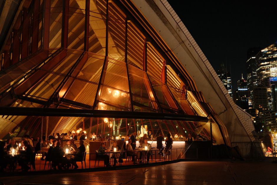 People dining inside the Sydney Opera House Opera Bar with a vibrant city night view.