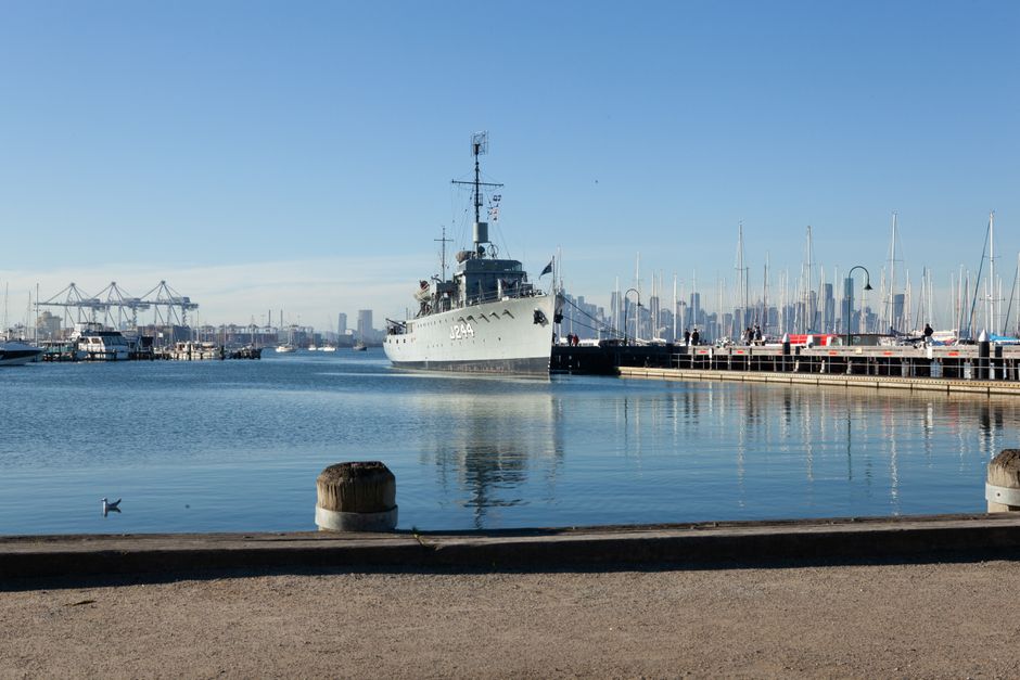 Navy ship docked in Williamstown, Victoria, with Melbourne skyline and clear blue sky.