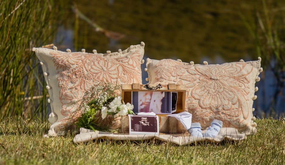 Rustic outdoor scene with decorative pillows, baby socks, and flowers, symbolizing a baby announcement celebration.