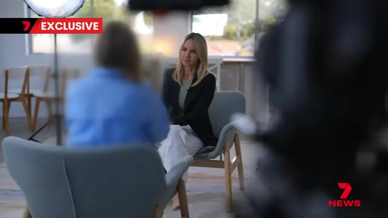 TV interview shot showing a woman seated across from an interviewer in a living-room style setting