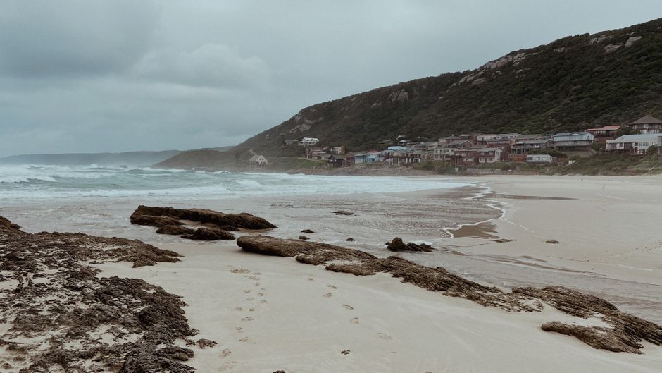 Dramatic coastline of Kareedouw with rocky beach and waves under a cloudy sky.