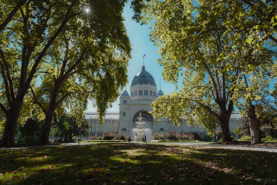 The Royal Exhibition Building in Melbourne surrounded by lush greenery under a clear blue sky.