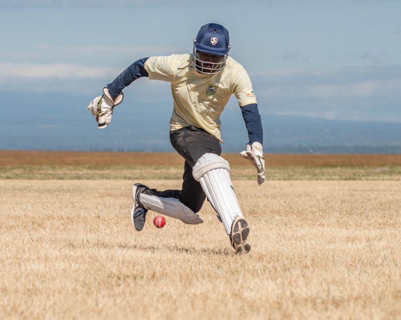 Cricketer skillfully fielding during an outdoor match on a sunny day.