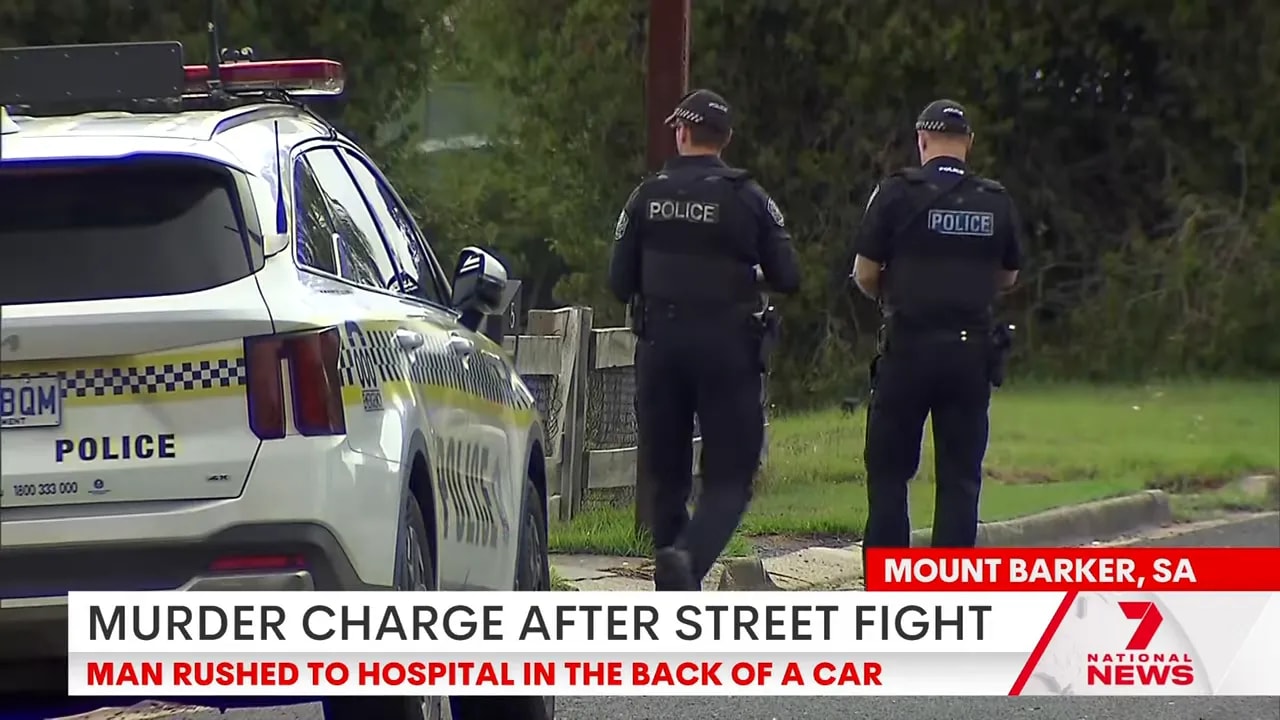 Two police officers walking beside a marked police SUV at a suburban scene with a news chyron about a murder charge.