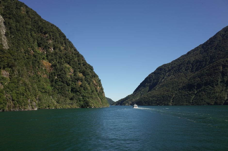 A boat navigates through the scenic waterway of Fiordland National Park, surrounded by lush green mountains.
