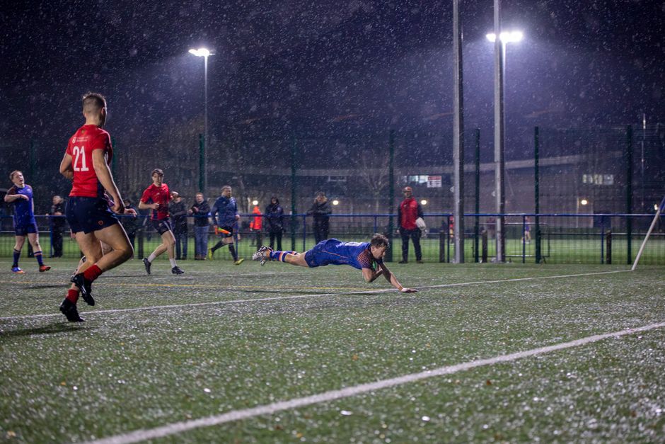 Intense rugby match in England with a player scoring a try in the rain.
