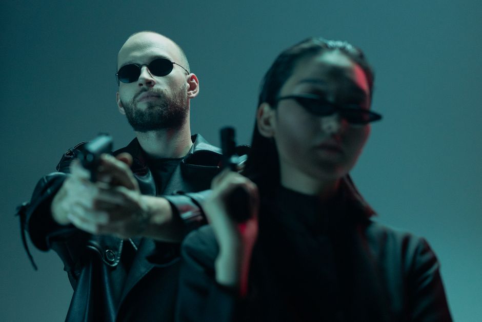A man and woman in sunglasses holding guns, showcasing a suspenseful scene.