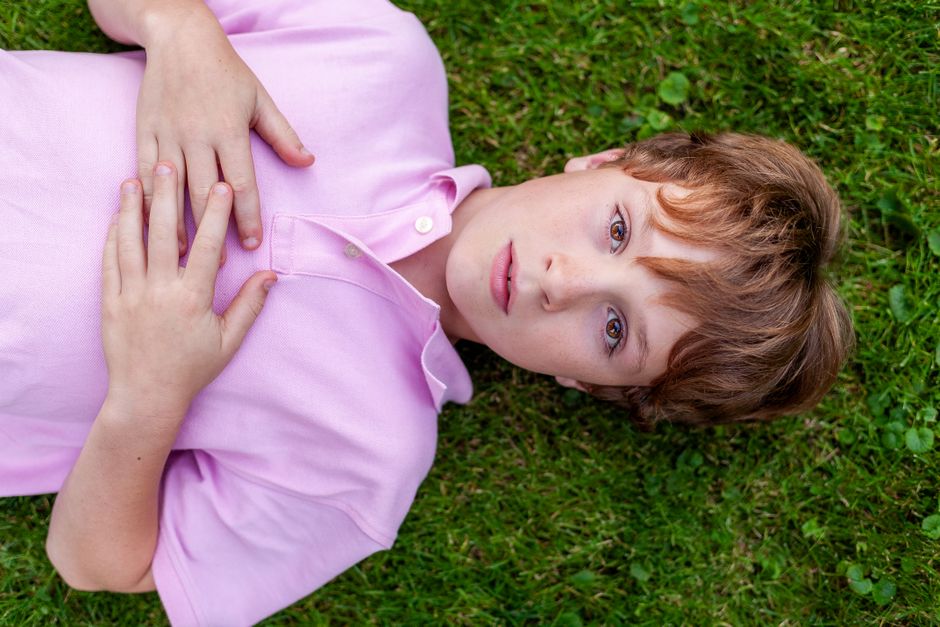 A young boy in a pink shirt lies on green grass, a serene expression on his face.