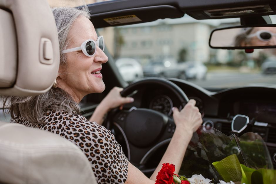 Senior woman driving a convertible, smiling and wearing sunglasses on a sunny day.