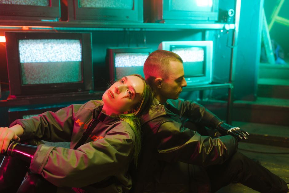 Futuristic cyberpunk atmosphere with young adults and prosthetics among retro TVs.