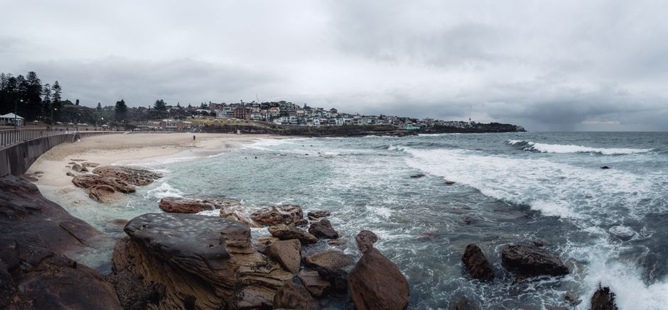 Panoramic scene of Bronte Beach with its rocky shore and cloudy sky in NSW, Australia.
