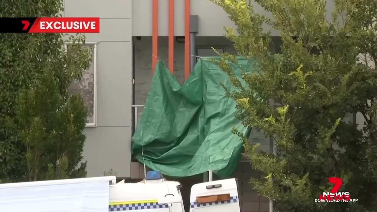 Green tarpaulin draped over an apartment entrance with police vehicles visible below